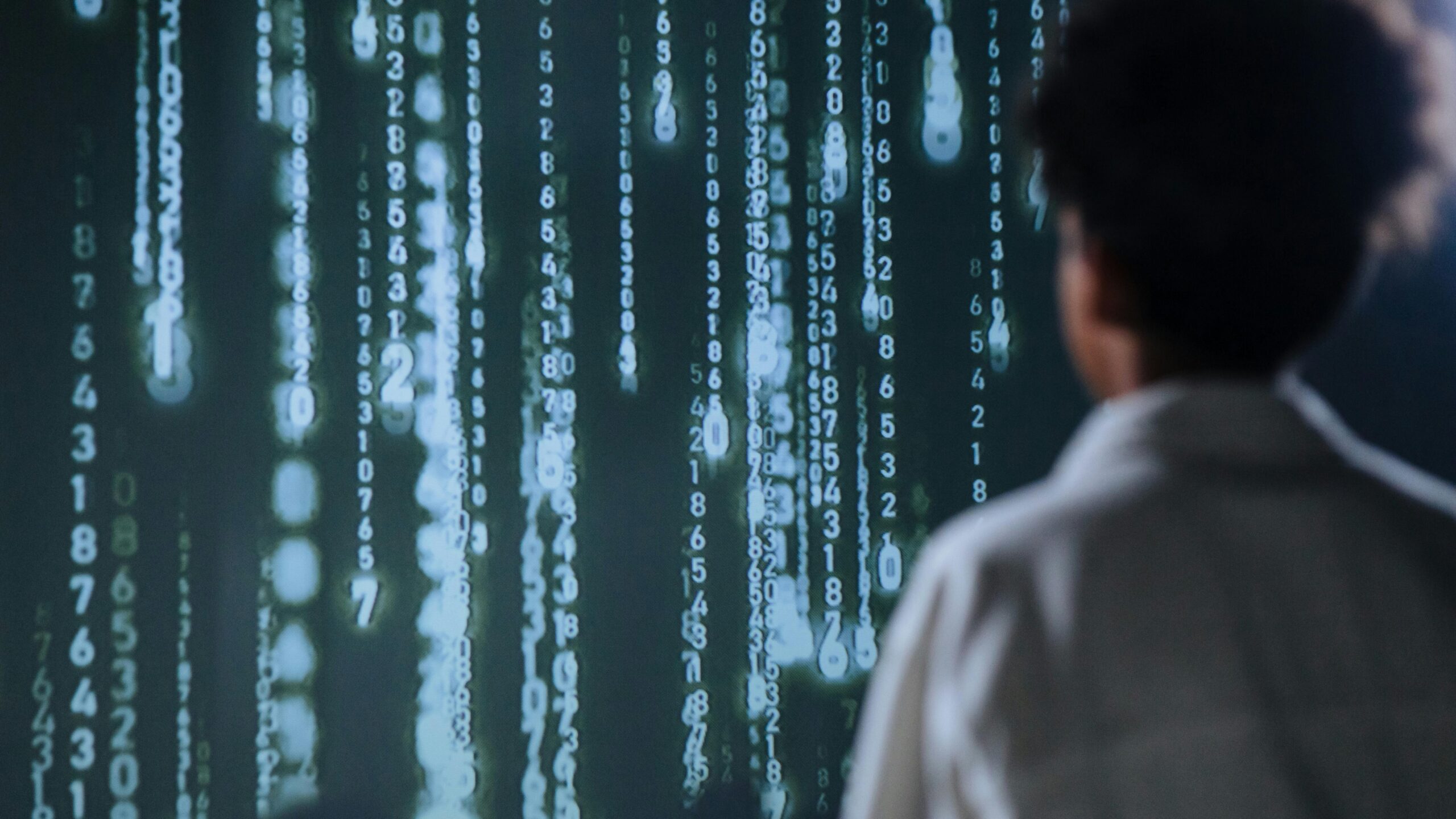 A person looking at a digital screen displaying streams of glowing binary and numeric code